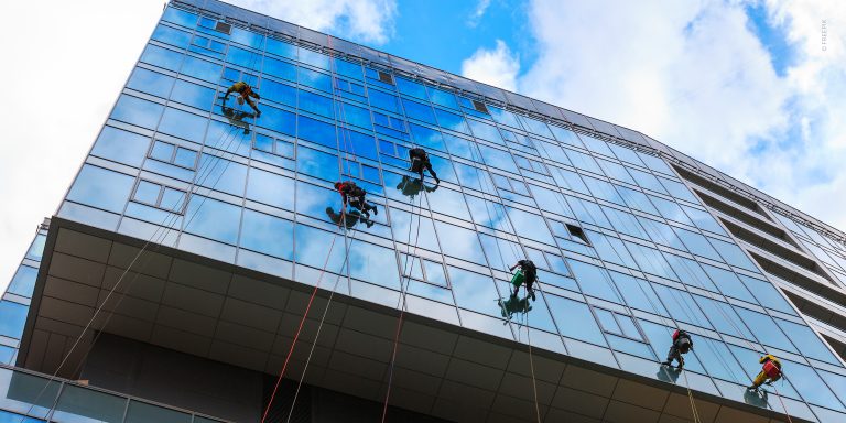 Modernes Bürogebäude mit Glasfassade wird von einem Team von Glasreinigern gesäubert. Die Glasreiniger-Fachkräfte verwenden dazu Seiltechnik, um die Reinigung der Fensterscheiben vorzunehmen.