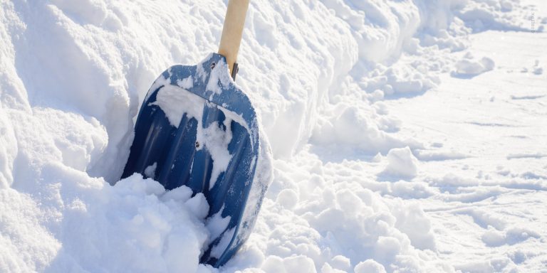 Eine Fläche mit Schnee wird im Rahmen der Dienstleistung Winterdienst mit einer blauen Schaufel vom Schnee befreit.